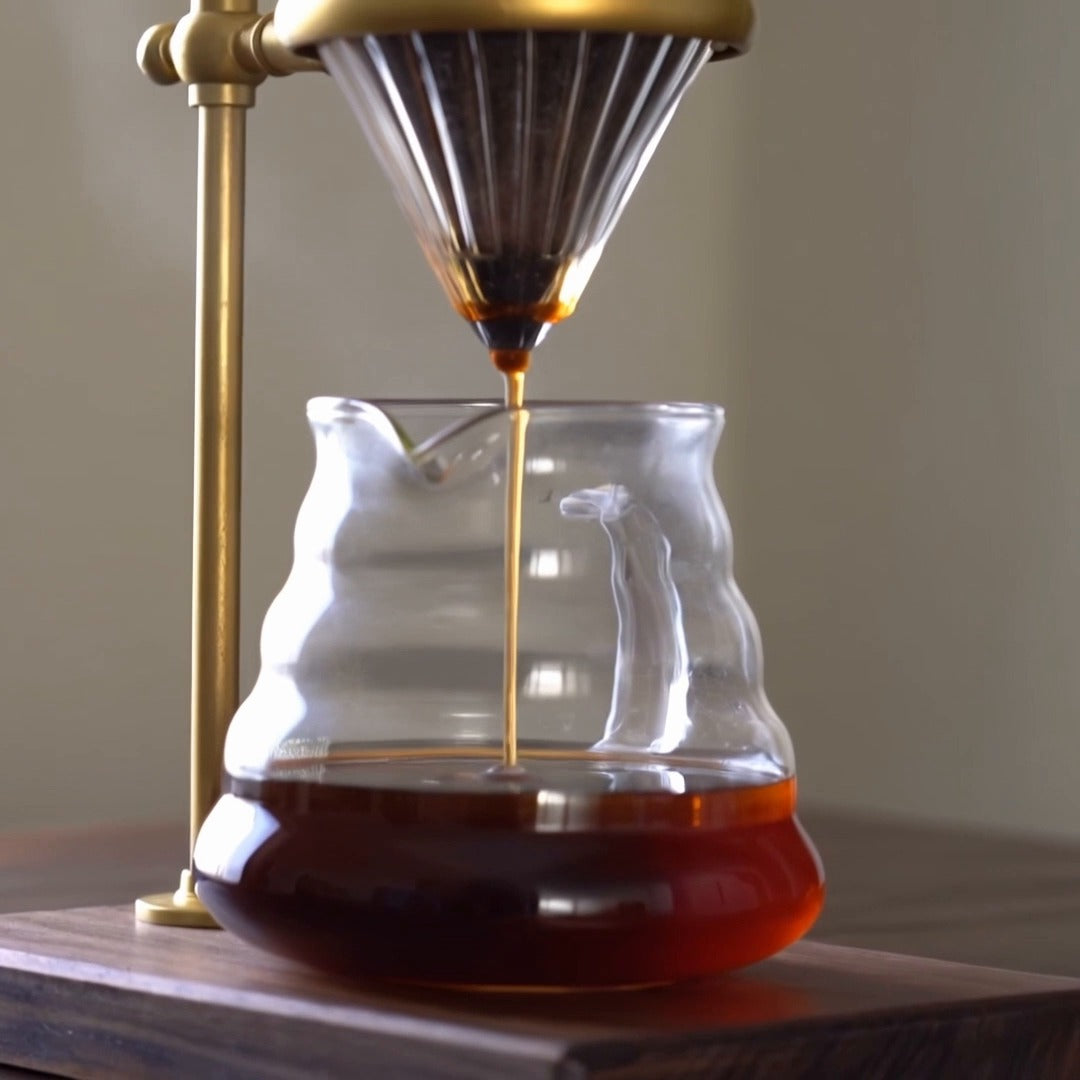 Coffee pouring into glass server on walnut base